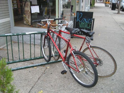 Two red bicycles in a bike rack on a sidewalk.